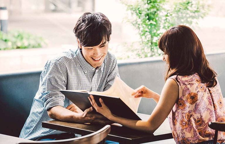 Man and woman sitting at a table while looking at a book and laughing