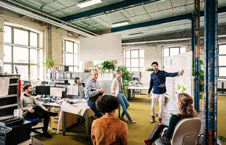 A group of people sitting in an office watching a man presenting in front of them