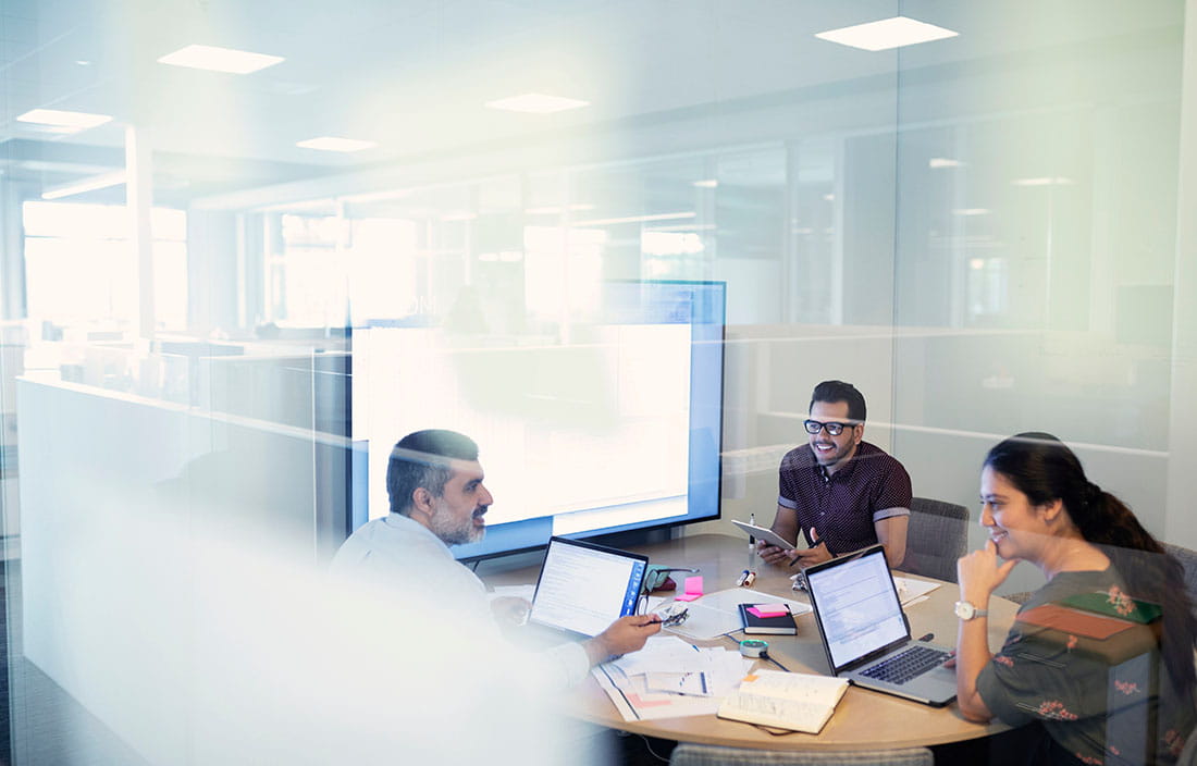 Group of people sitting around a desk with their laptops