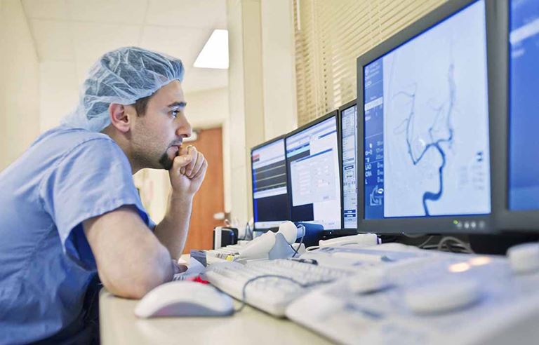 Doctor in scrubs viewing medical information on a computer monitor.