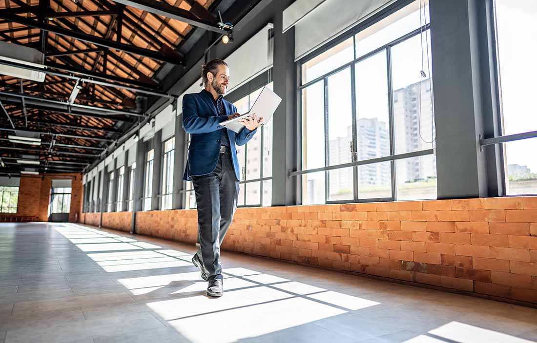 Real estate professional walking in a warehouse and reading about tax insights on their laptop.