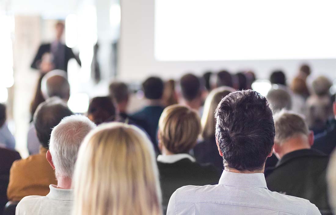 Audience of plastics professionals listening to a speaker presenting.