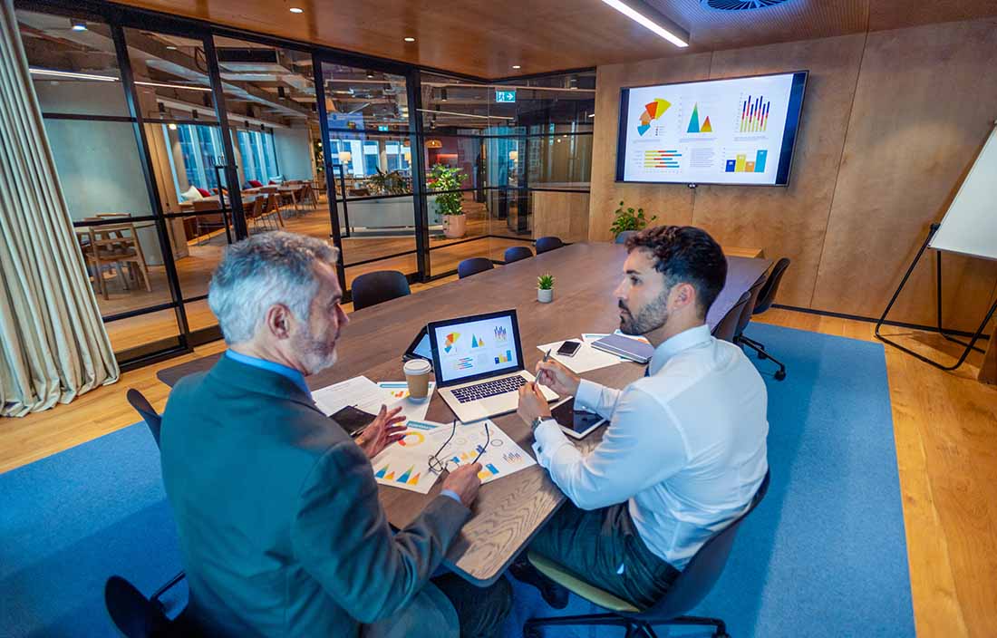 Two for-profit healthcare professionals sitting in a modern conference room reviewing charts.