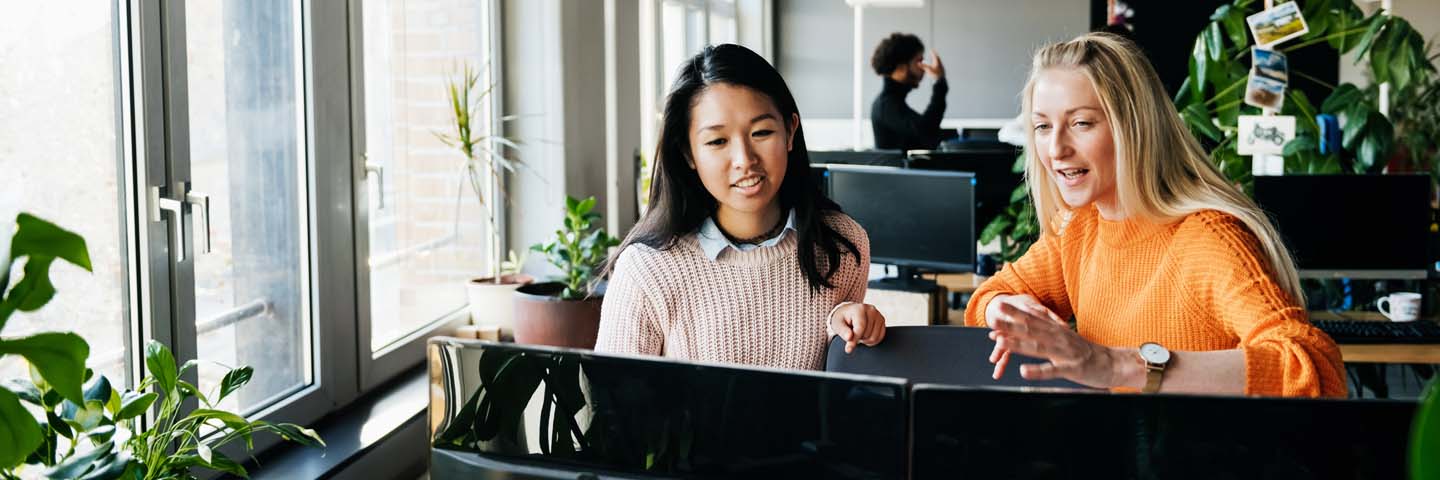 Two business professionals sitting at their desk in a modern office learning about generative AI.