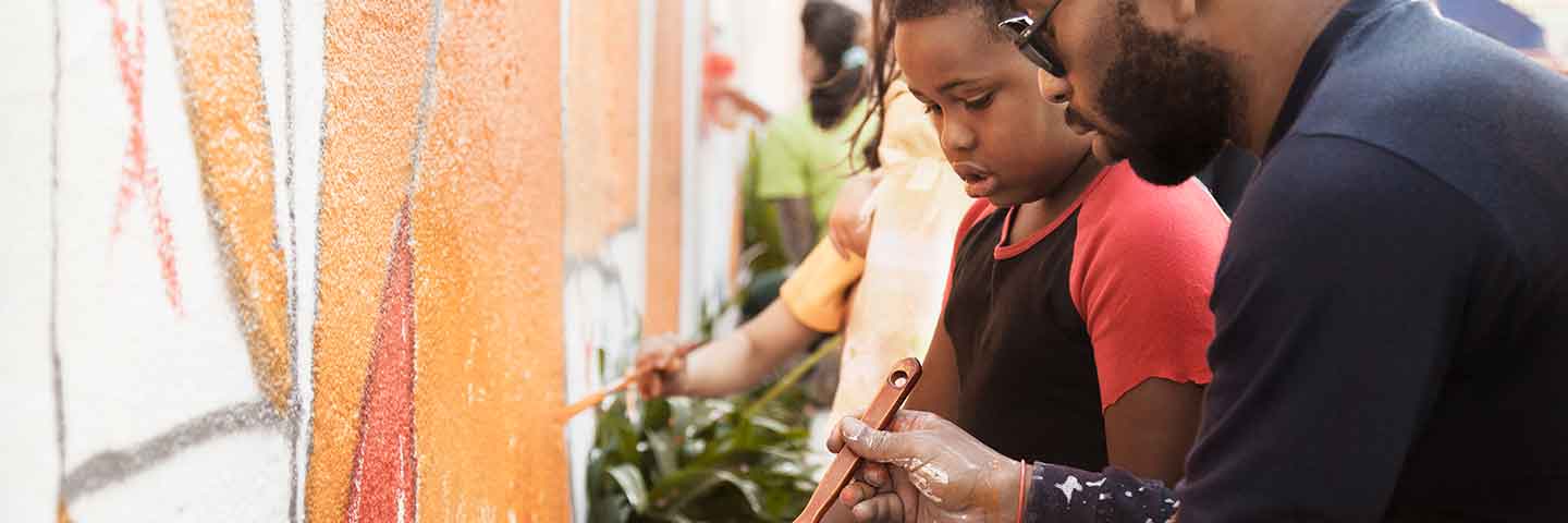 Adult helping a child to paint a mural.