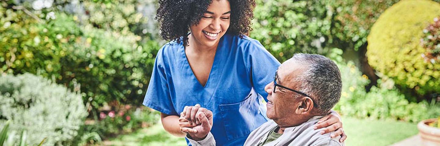 Nurse smiling and helping senior citizen in a garden.