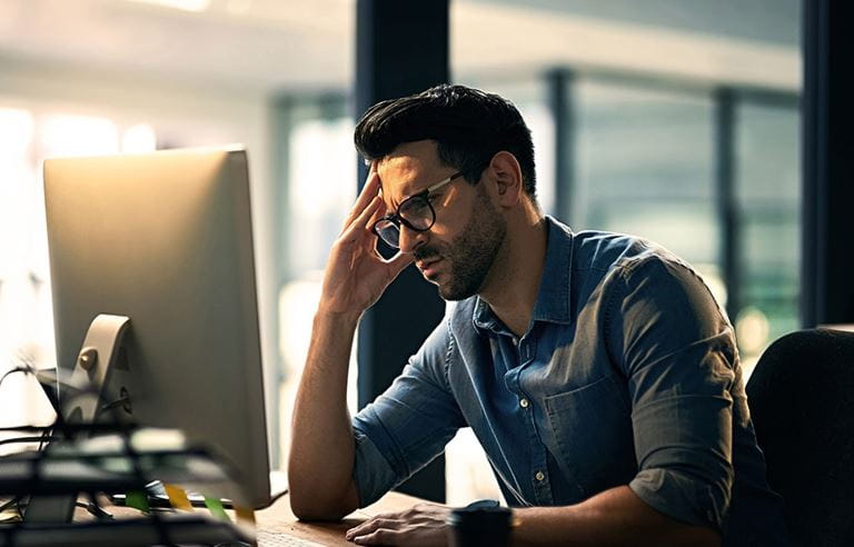 A picture of a man sitting at a desk who is worried and suspects fraud. 