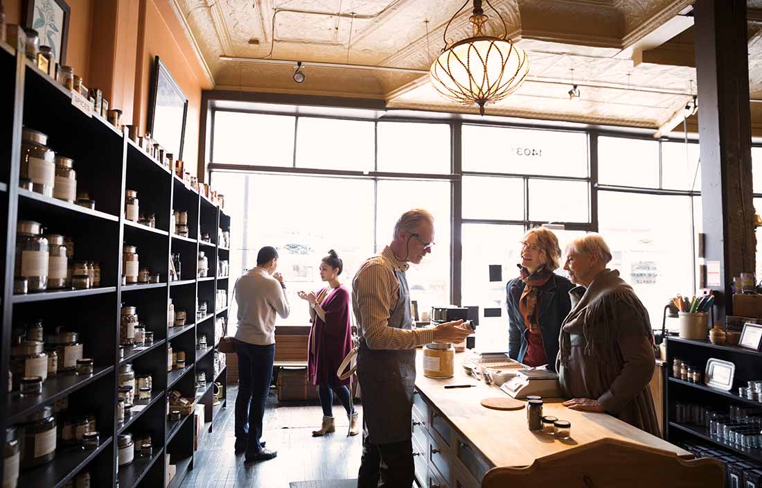 Image of the inside of a small shop with shelves of glass jars and a male cashier assisting two women.