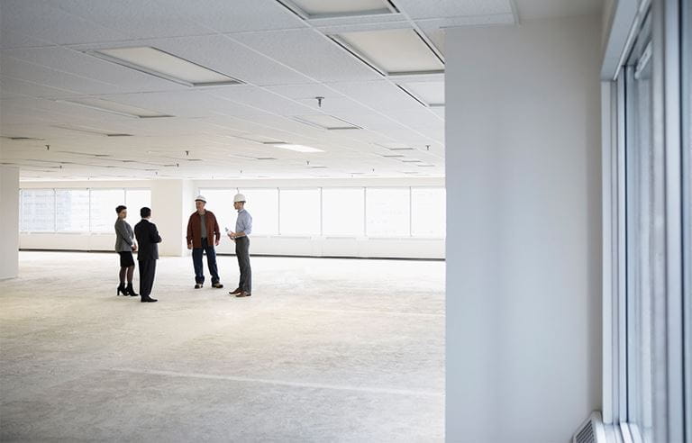 Two business professionals discussing office floor plans with two construction workers. 