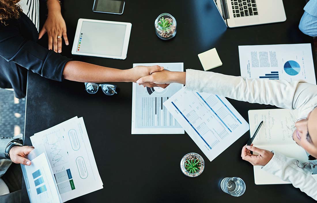 Business colleagues shaking hands while sitting at a conference table. 