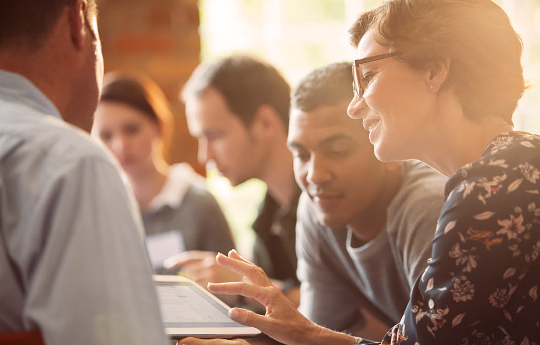 Multiple people sitting at a table looking at a tablet