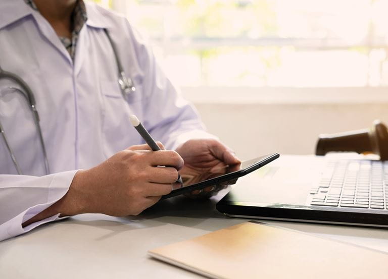 Doctor sitting at a desk, writing on a tablet.