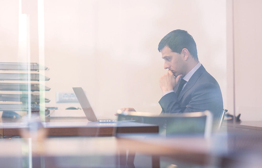 Businessman sitting at wooden desk looking at his laptop computer intently.