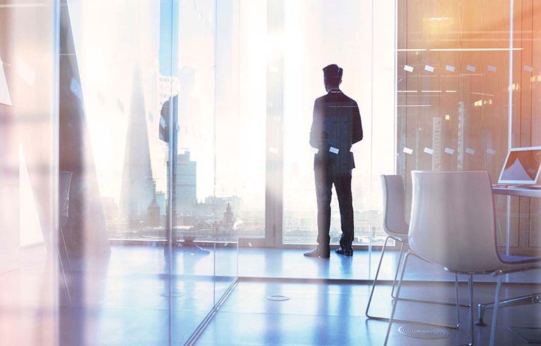 A business executive standing by an all glass wall looking into the city.