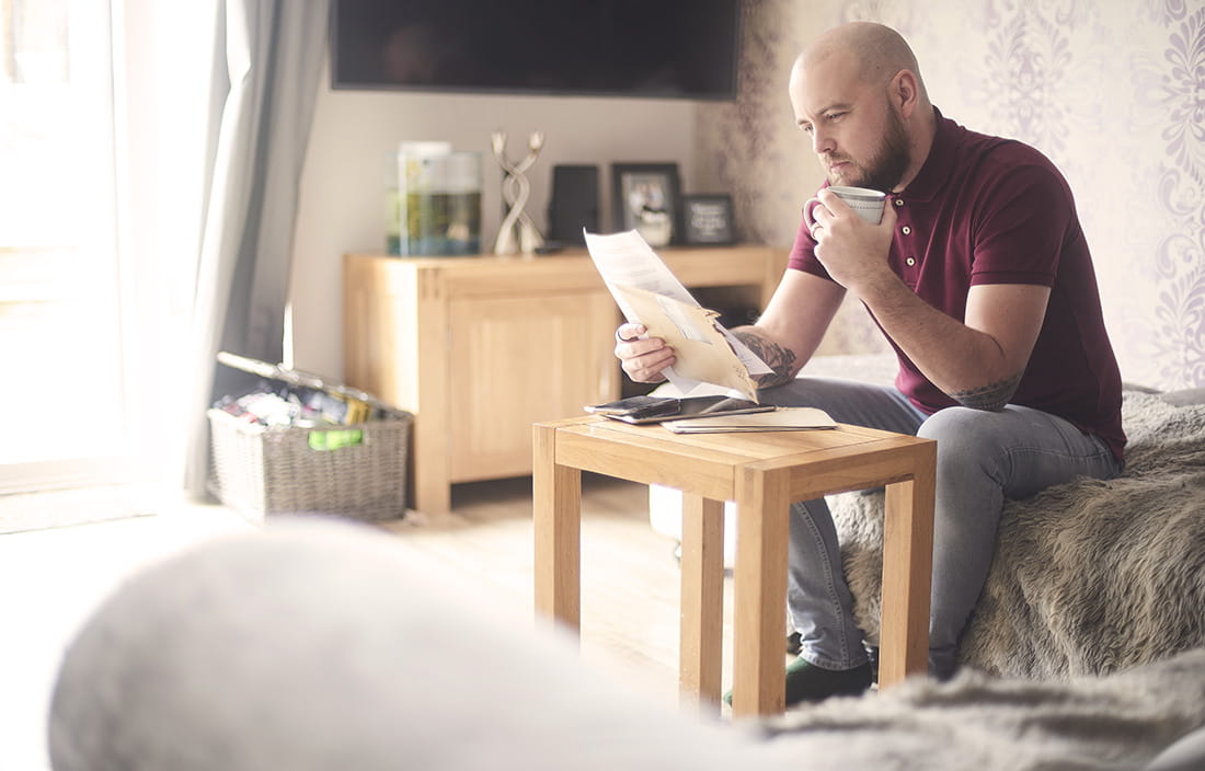 Younger man sitting on couch reading an FAQ about the Paycheck Protection Program.