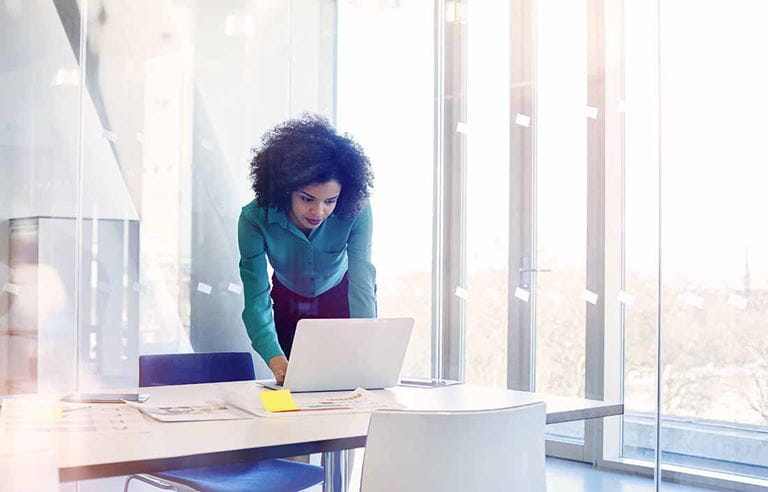 Young businesswoman leaning over a table using a laptop computer.