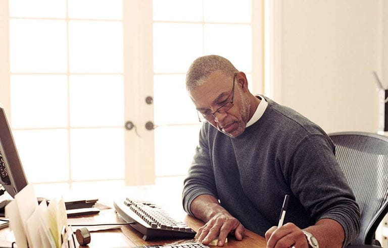 Man sitting at his home office desk writing with a pen.