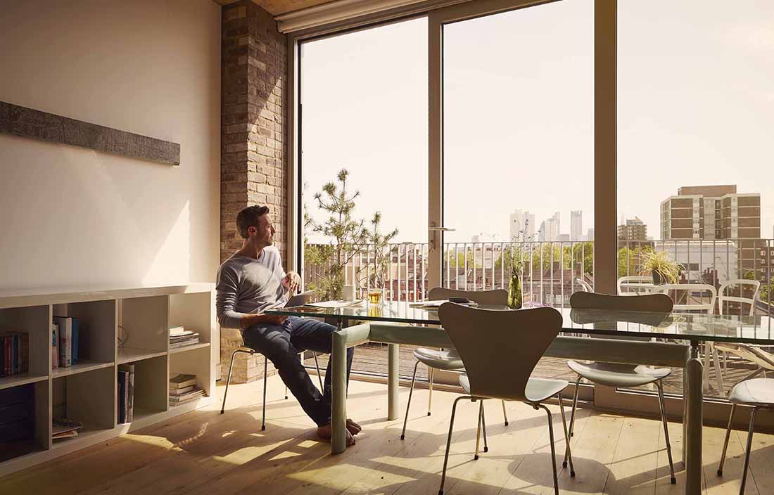 Man sitting at a modern glass kitchen table looking out the window.