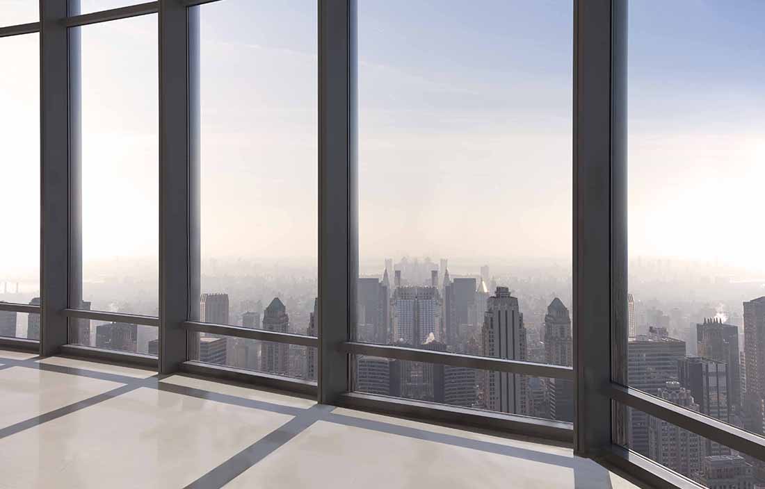 The view out of a very tall glass skyscraper, looking down on other buildings