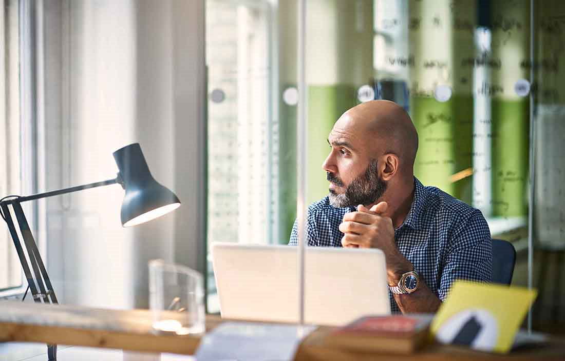 Businessman sitting at his desk in casual business clothes looking out his office window.