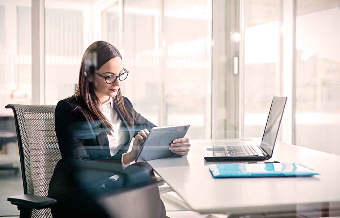 Businesswoman sitting at a desk using a tablet handheld device.