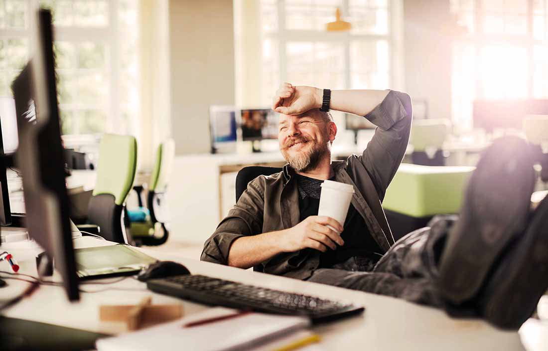 Worker in casual clothes leaning back in office chair laughing.