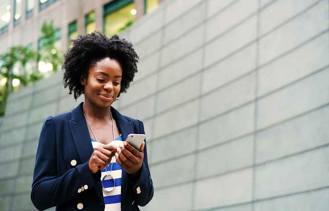 Businesswoman smiling and looking down at her phone in an outdoor area.