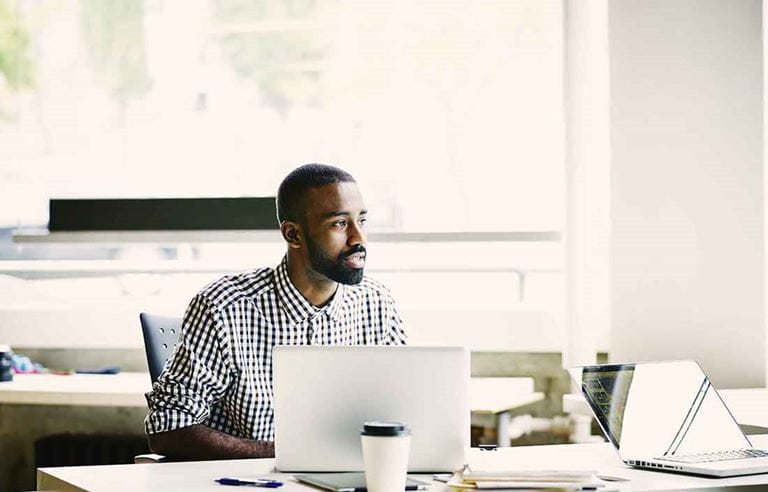 Businessman looking off in the distance while sitting at his modern desk with two laptops on it.