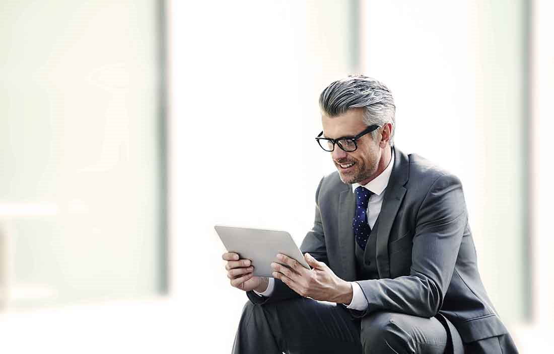 Businessman smiling while using a tablet handheld device.