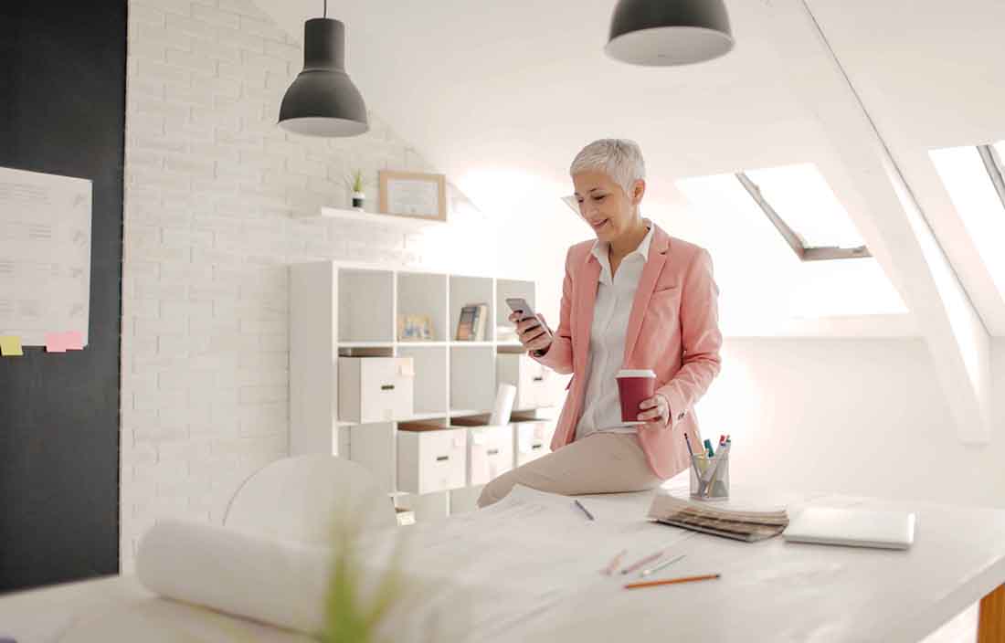 An elderly businessperson leaning against a white table checking their cell phone.