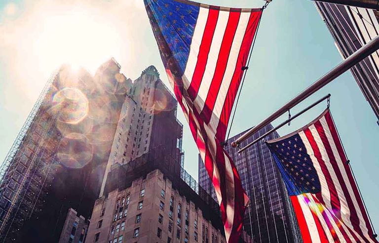 Close-up view of the American flag with skyscraper buildings in the background.