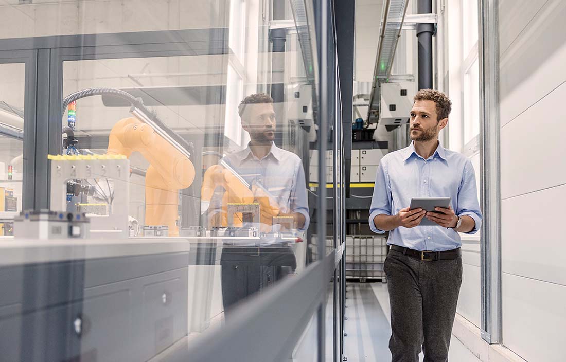 Businessman walking through a modern factory while holding a handheld tablet device.