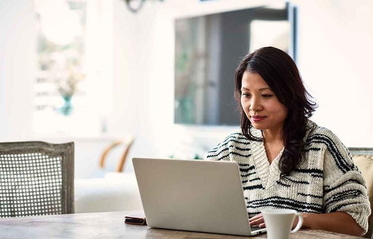 Woman wearing a sweater using a laptop computer at the kitchen table.