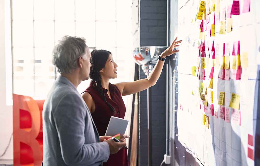 Businesswoman pointing at a board with post-it notes stuck to it.