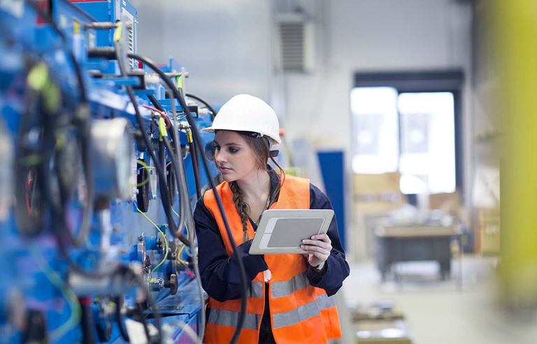 Worker wearing a protective hard hat checking manufacturing machinery.