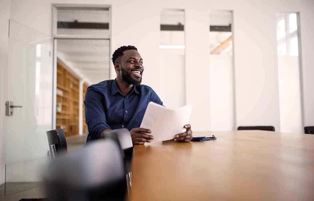 Business professional sitting at a conference room table holding a piece of paper and smiling.