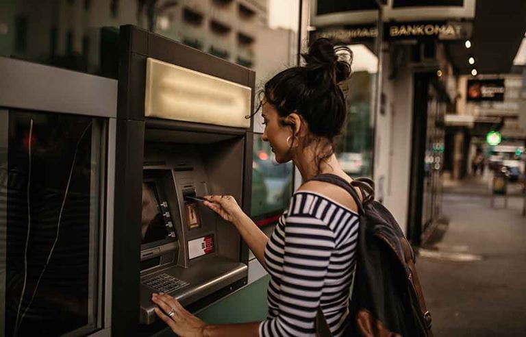 Younger adult using an ATM machine on the street to withdraw money.