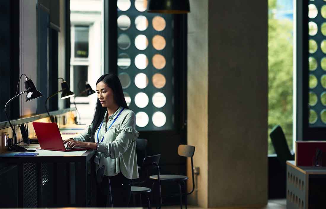 Business professional sitting at their desk using a red laptop computer on the desk.