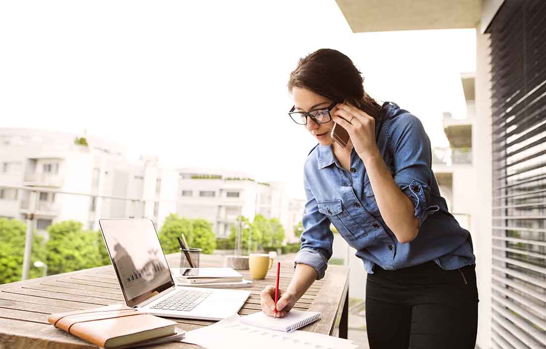 Business professional taking a phone call while taking notes on a notepad.