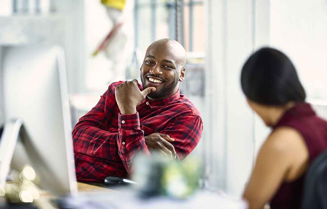 Two business professionals in an office discussing something together at their desks.