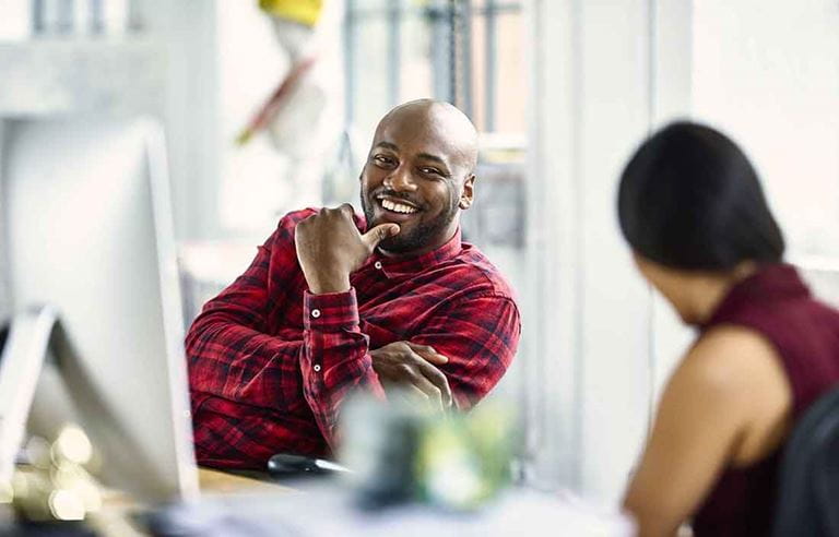 Two business professionals in an office discussing something together at their desks.