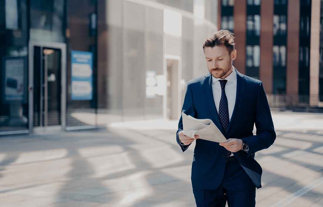 Business professional standing outside reading a newspaper.