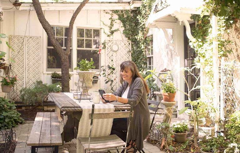 A middle aged person sitting at an outdoor table using their cell phone.