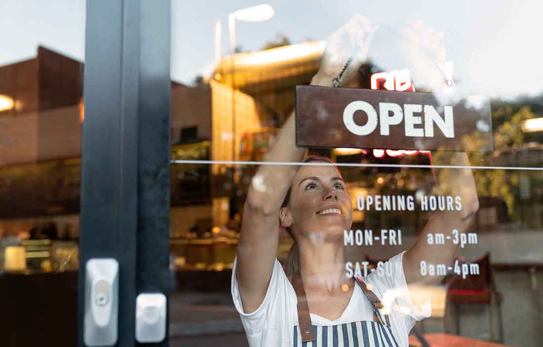 Store owner hanging an open sign in the front window.