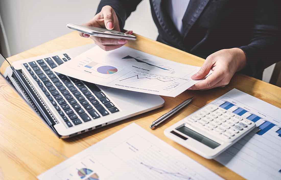 Close-up view of a business professionals hands holding their cellphone and documents with charts.