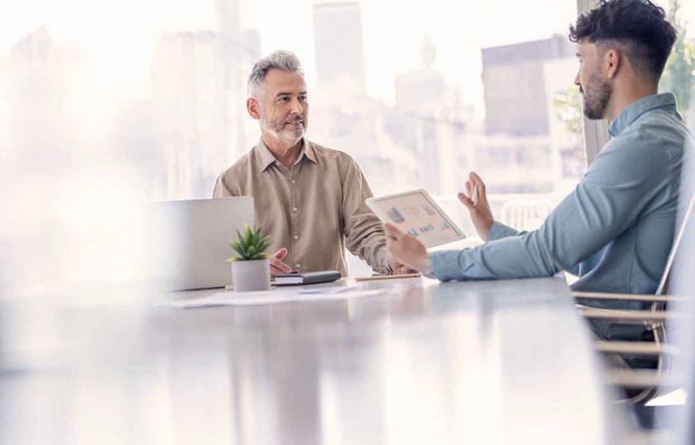 Two business professionals sitting at a table discussing information on a tablet device.