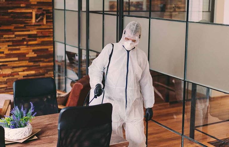 Man in protective gear/hazmat suit cleaning an office.