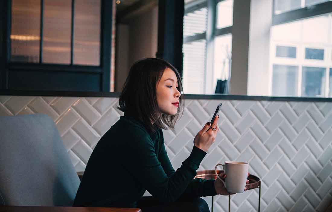 Business professional using their phone and drinking coffee.