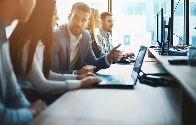 Group of business professionals sitting together at a table with their laptops out.