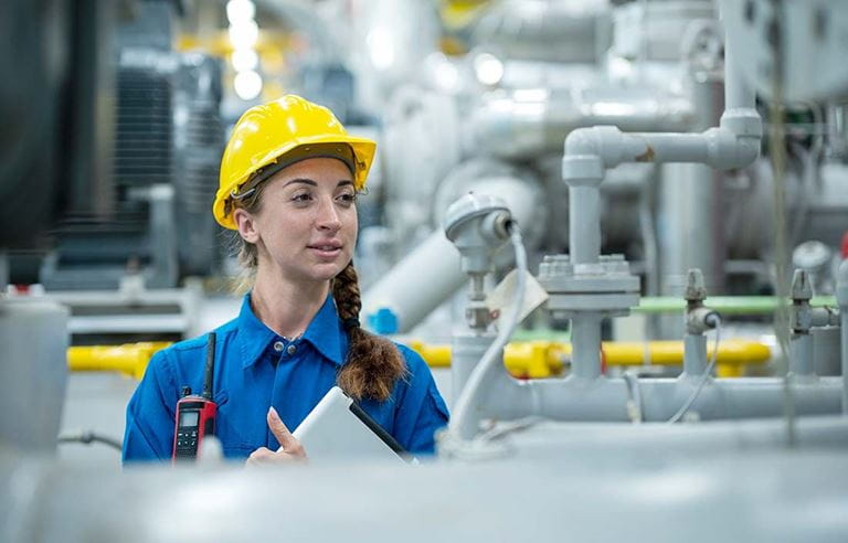 Factory worker wearing a hard hat inspecting factory lines.